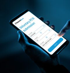 A person holding a smartphone in one hand and using the other hand to tap the “Submit” button on a mobile screen displaying a “Voluntary PCN submission” form from Chemius, with fields for VAT number, Formula ID, and UFI number, against a dark blue background