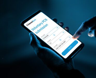 A person holding a smartphone in one hand and using the other hand to tap the “Submit” button on a mobile screen displaying a “Voluntary PCN submission” form from Chemius, with fields for VAT number, Formula ID, and UFI number, against a dark blue background