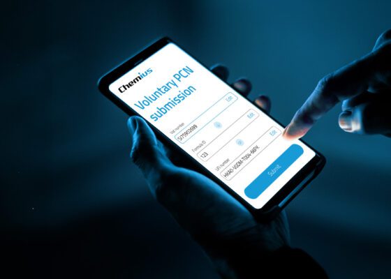 A person holding a smartphone in one hand and using the other hand to tap the “Submit” button on a mobile screen displaying a “Voluntary PCN submission” form from Chemius, with fields for VAT number, Formula ID, and UFI number, against a dark blue background